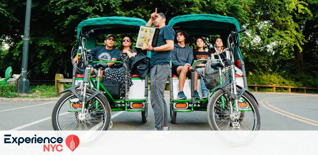 A group of people enjoys a pedicab tour in a park setting. Two green pedicabs with passengers are parked on a paved path surrounded by lush trees. A tour guide stands in front, holding a booklet in one hand and gesturing with the other. Bright and lively outdoor atmosphere, conveying a sense of exploration and enjoyment. Experience NYC logo is visible at the bottom, adding a local context to the image.