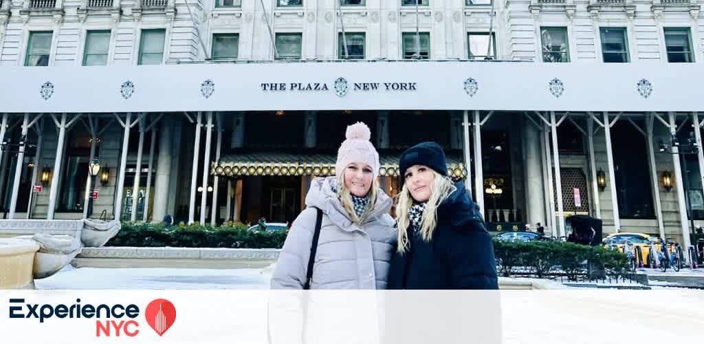 Two people are standing in front of The Plaza Hotel in New York City. They are dressed warmly in coats and hats, suggesting a chilly day. The hotel’s grand facade is visible in the background, showcasing its iconic architecture. The logo Experience NYC is displayed in the bottom left corner of the image. The scene conveys a sense of urban exploration and tourism in a famous location.