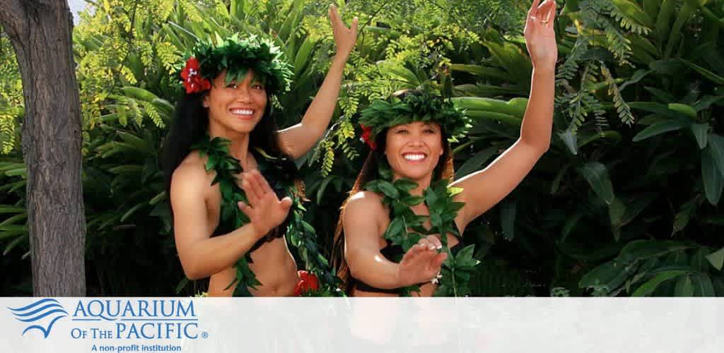 Two dancers in traditional attire with green foliage and red flowers, performing in front of lush tropical plants.