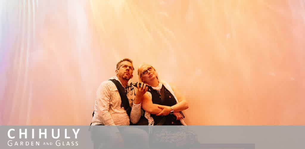 Two people sitting on a bench, gazing at an abstract, warm-colored background.