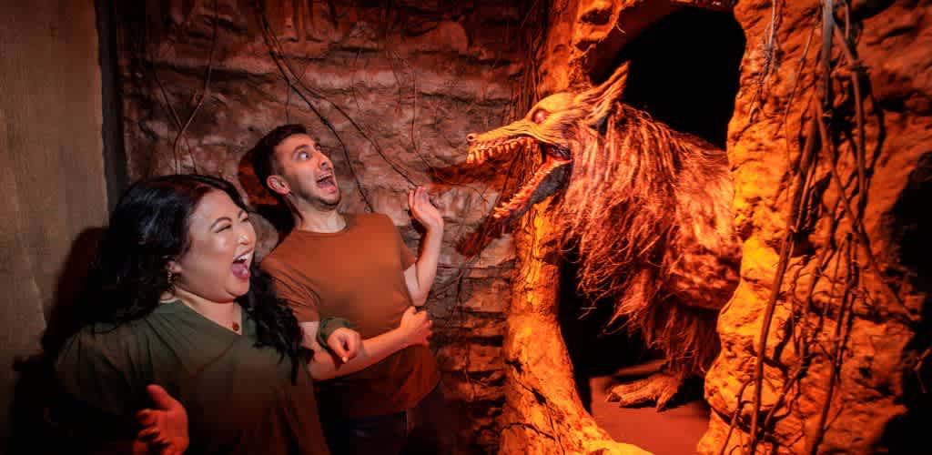 Two guests scream as a werewolf prop lunges from a wall inside a dimly lit haunted maze.