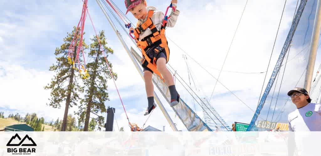 A child on a bungee trampoline, suspended in the air, with trees and a clear sky in the background.