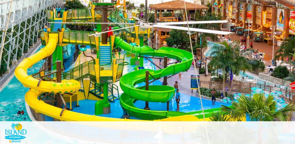 Vibrant indoor water park scene with a large, winding water slide in yellow and green. Palm trees and tropical plants create an island atmosphere. Visitors enjoy swimming and lounging in the water. The background shows a spacious seating area and a food court, all under a vast glass ceiling that allows natural light to illuminate the area.