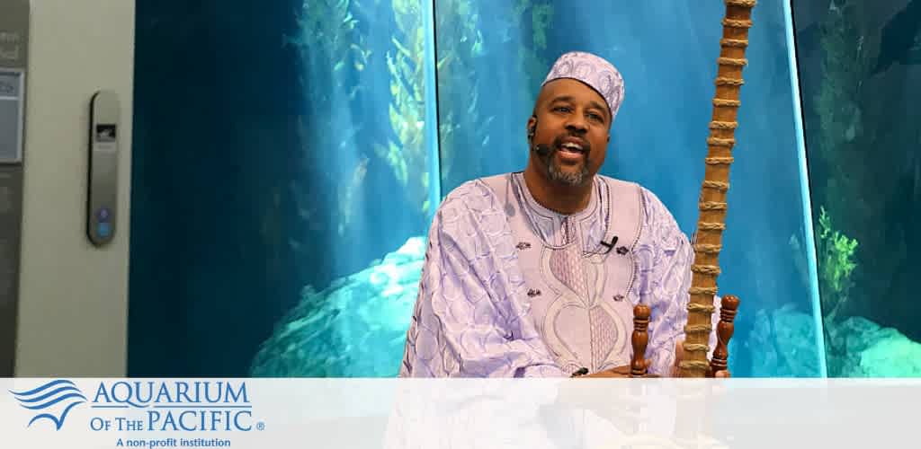 Man in traditional attire seated in front of an aquarium tank at the Aquarium of the Pacific.