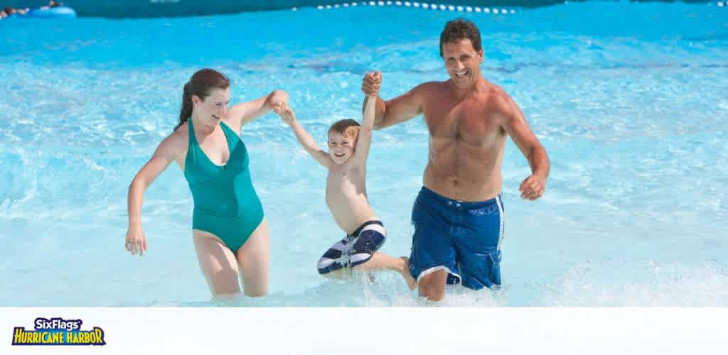 A woman, a young boy, and a man playing in a pool, holding hands and smiling.