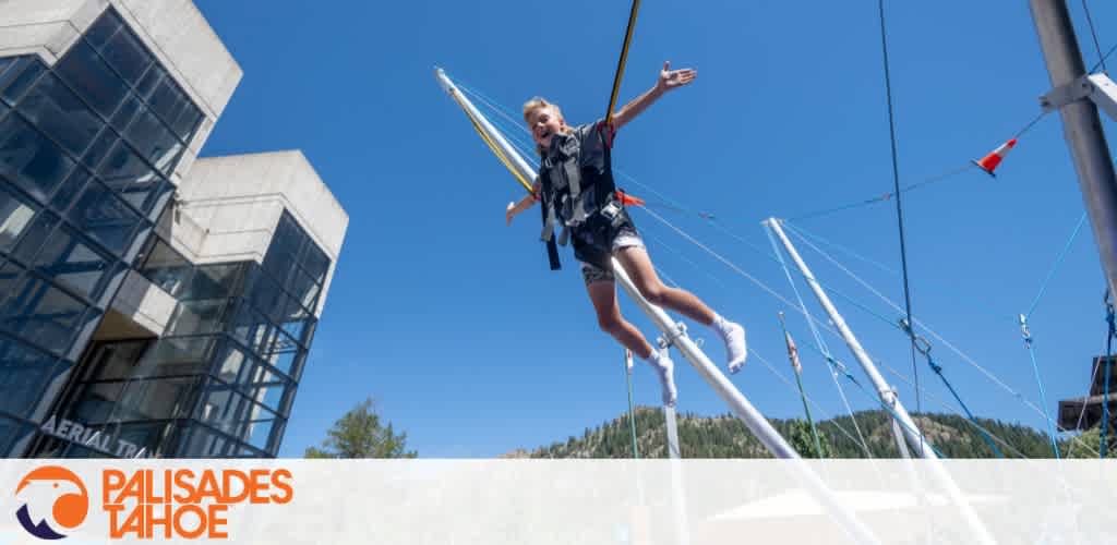 A person jumping on a bungee trampoline with blue sky and a glass building in the background.