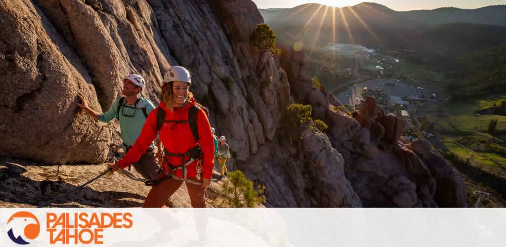 Climbers ascending a rocky mountain at sunrise or sunset with a scenic valley in the background.