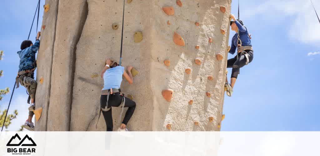 Three people rock climbing on a large artificial wall with safety ropes on a sunny day.