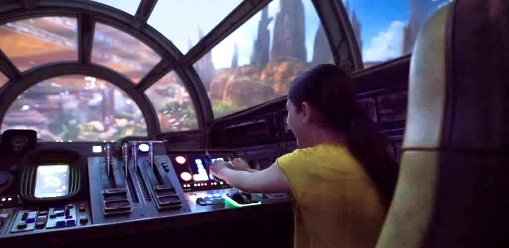A woman sits in the cockpit of a Star Wars vehicle, focused on the controls and surrounded by futuristic instruments.