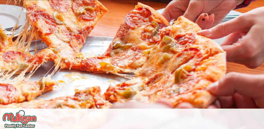 Hands pulling slices from a pepperoni and green pepper pizza.
