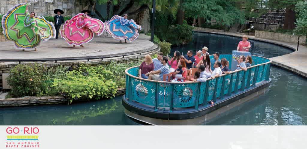 Dancers in colorful traditional dresses perform by a riverside as a boat filled with people floats by.