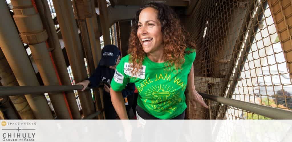 A woman in a green t-shirt climbing metal stairs, smiling.