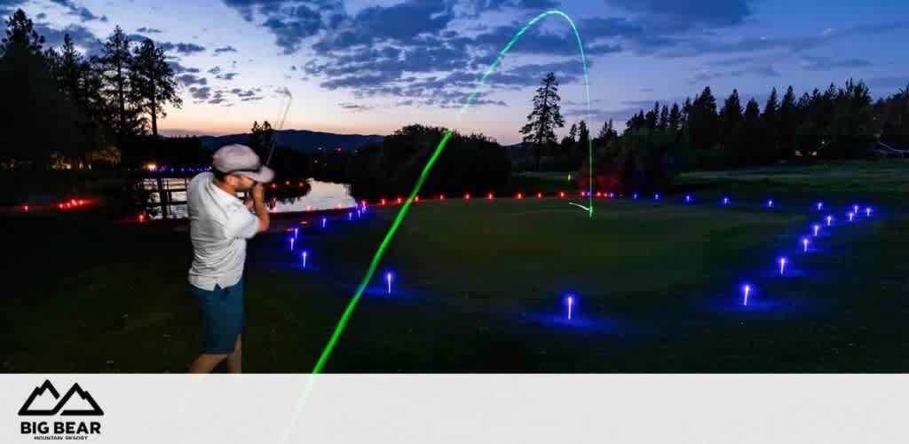 Golfer swinging at night on an illuminated course with LED lights and a visible ball trajectory arc.