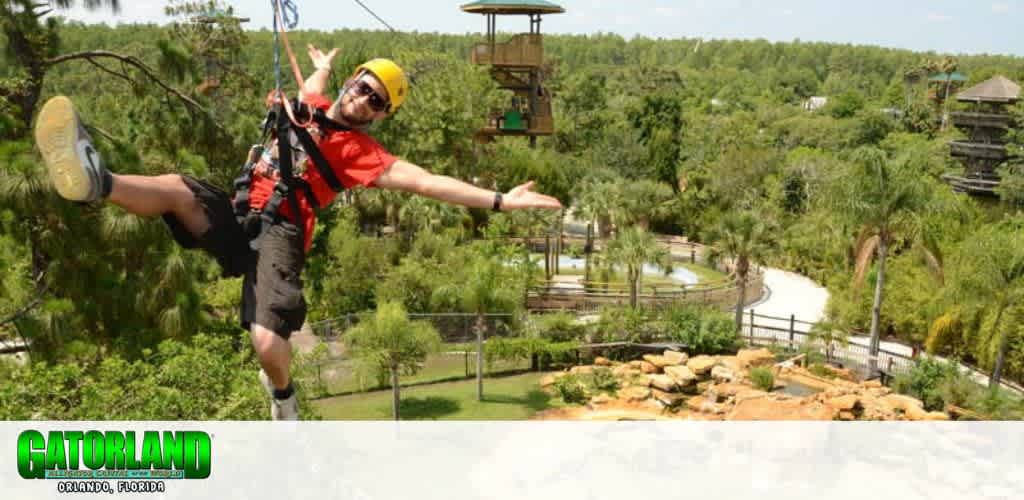 A person is joyfully zip-lining through a lush, green park. They're wearing a helmet and harness, with trees and wooden observation towers visible in the background. The scene conveys a sense of adventure and fun in the outdoors, perfect for thrill-seekers. The foreground features a water feature with rocks and foliage, adding to the scenic beauty.