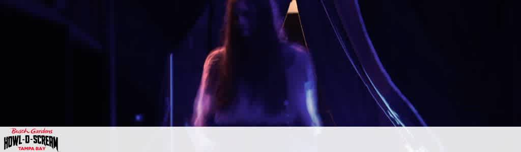 A person with long hair on stage performing with colorful neon lights surrounding them at a concert or event.