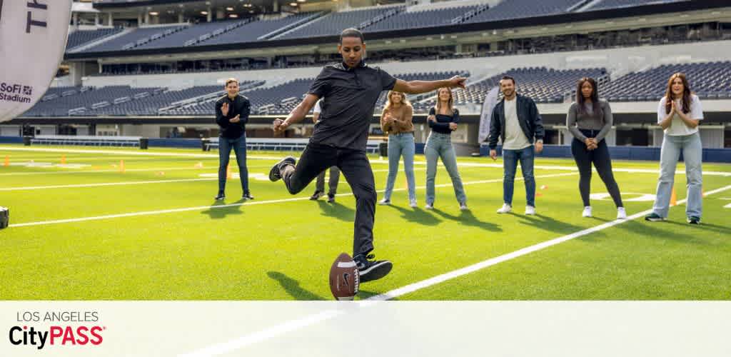 Group of diverse people watching a person kick a football on a stadium field during daytime