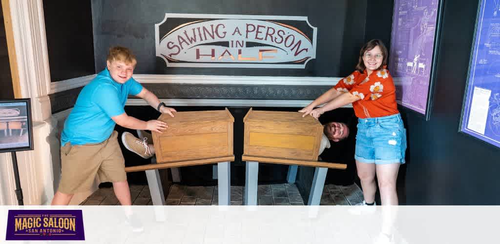 Three children smiling and pushing wooden boxes in a fun museum exhibit titled Sawing a Person in Half at Magic Saloon San Antonio