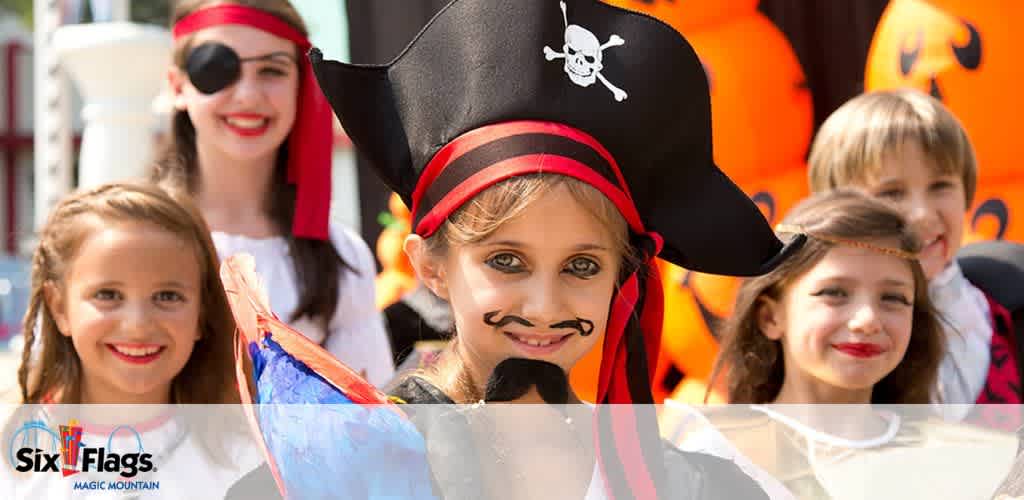 A group of children in Halloween costumes, with a child dressed as a pirate in the foreground, featuring pumpkins in the background.