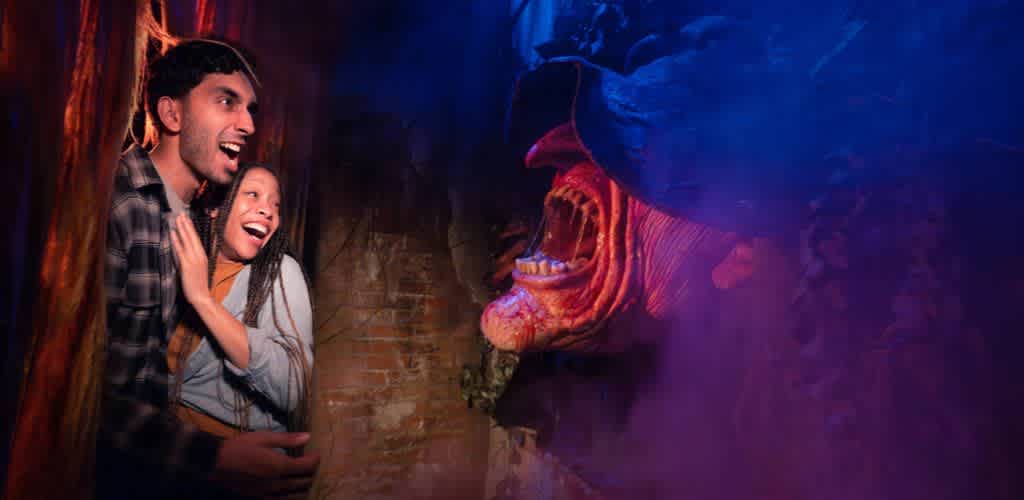 A man and girl are surprised by a large, colorful dragon prop in a dark indoor setting with orange and purple lighting.