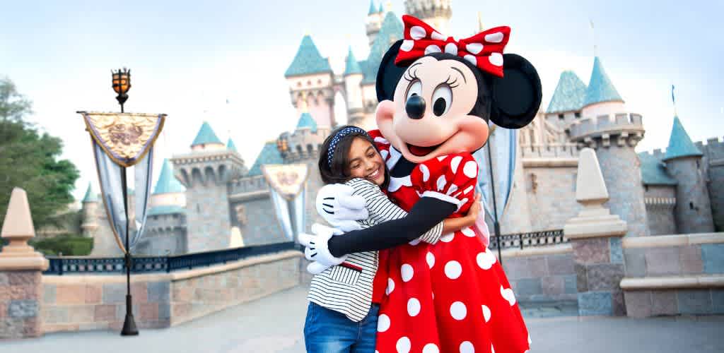 A young girl hugging Minnie Mouse in front of a disney castle at a theme park.