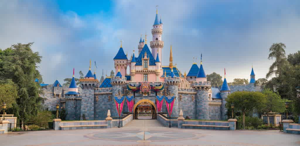 A colorful Disney castle with blue turrets, pink accents, and a welcoming entrance, surrounded by trees and a clear blue sky