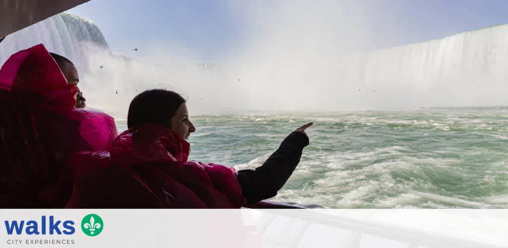 Two people sitting on a boat overlooking Niagara Falls, with one person pointing toward the waterfall during daytime