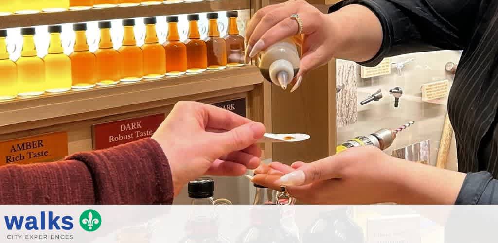A person hands a customer a small tasting spoon filled with syrup at a tasting station with bottles of syrup in the background.