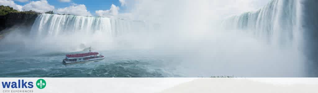 A boat sailing near the waterfalls of Niagara Falls with mist rising and surrounding green trees, showcasing a scenic natural landscape