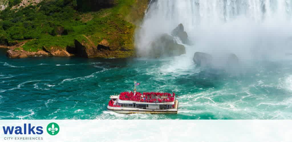 A boat tour near a large waterfall with lush green cliffs and mist rising over the water surface.