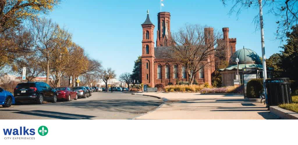 A historic red brick building with a tower and dome, surrounded by trees and parking lot on a sunny day