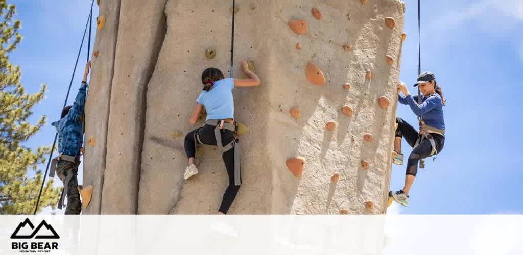 Three people climbing an artificial rock wall outdoors at Big Bear Mountain Resort.