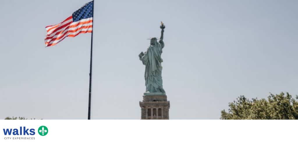 Statue of Liberty standing with an American flag flying nearby on a clear day with trees in the background