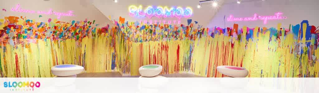 Colorful abstract mural with neon text and three white seating stools at a creative fun space