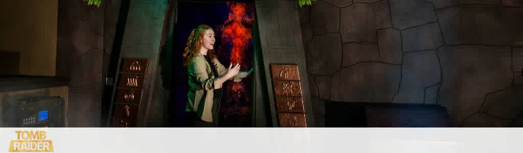 A woman interacts with a virtual exhibit in a dark themed museum setting with stone wall backgrounds and decorative panels.