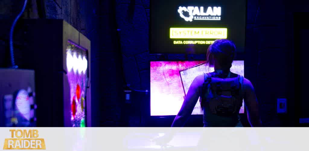 A person with a backpack is looking at a digital screen in a dark room illuminated by colorful lights and signs.