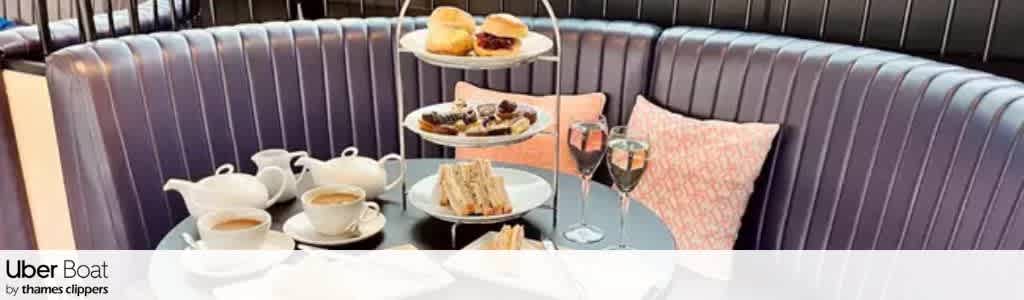 A curved booth with a table set for afternoon tea including tea, sandwiches, pastries, and two glasses of wine, with a pink cushion on the seat.
