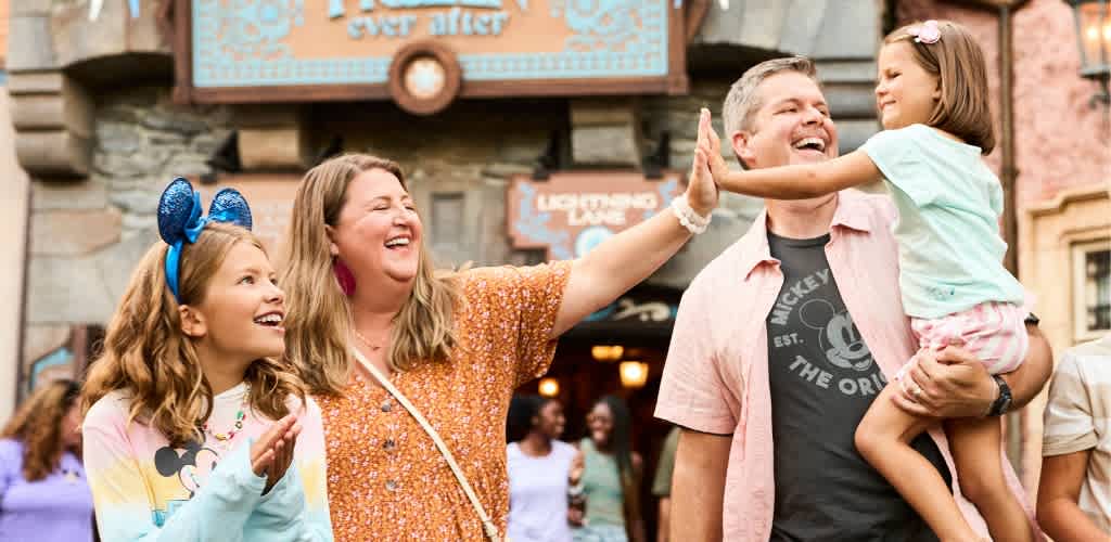 Family enjoying a joyful moment outdoors at a theme park with a woman and children smiling and high-fiving.