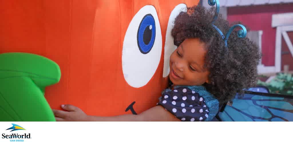 A child hugs a large, plush pumpkin figure with cartoon eyes.