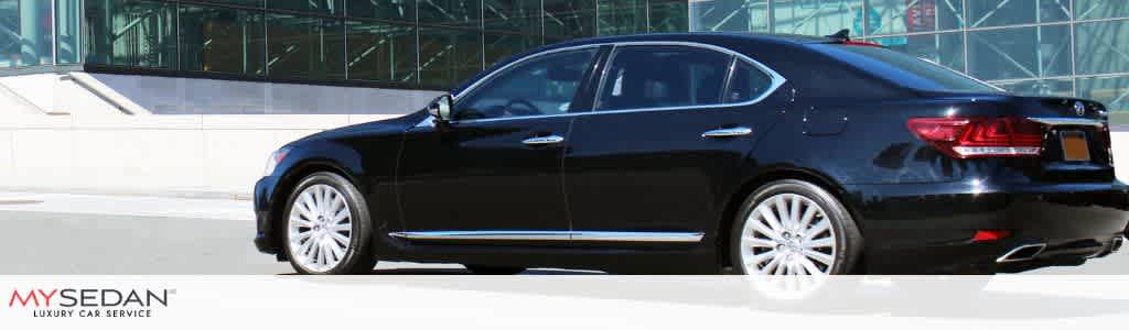 A black luxury sedan parked outside a modern building with glass windows and a white concrete wall