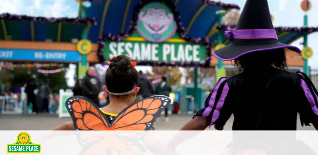 Two children dressed as a butterfly and a witch walking towards Sesame Place entrance on a bright day