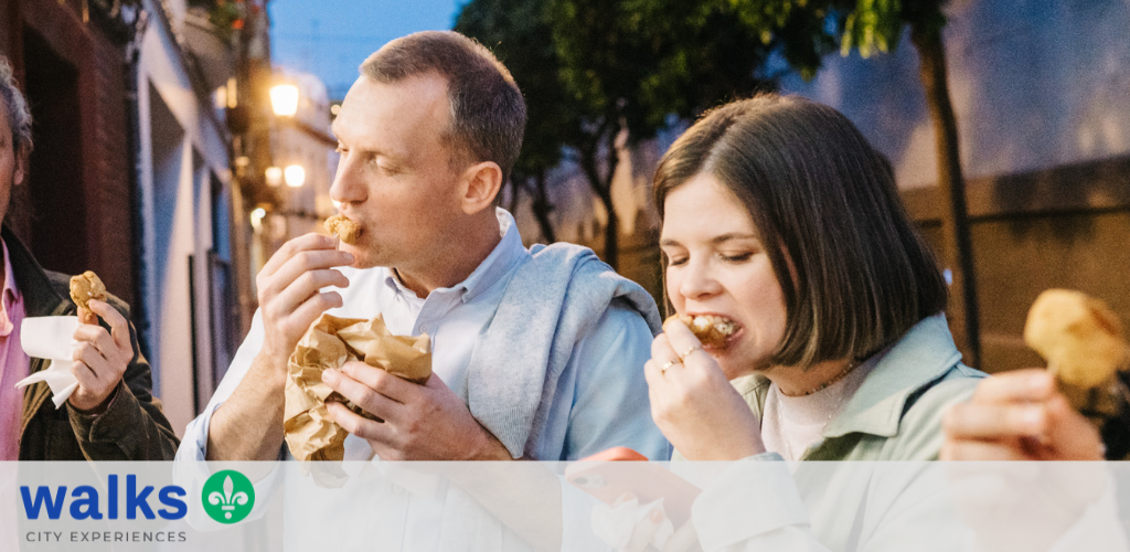 Two people eating fried chicken outdoors during the evening, enjoying a casual social moment together.