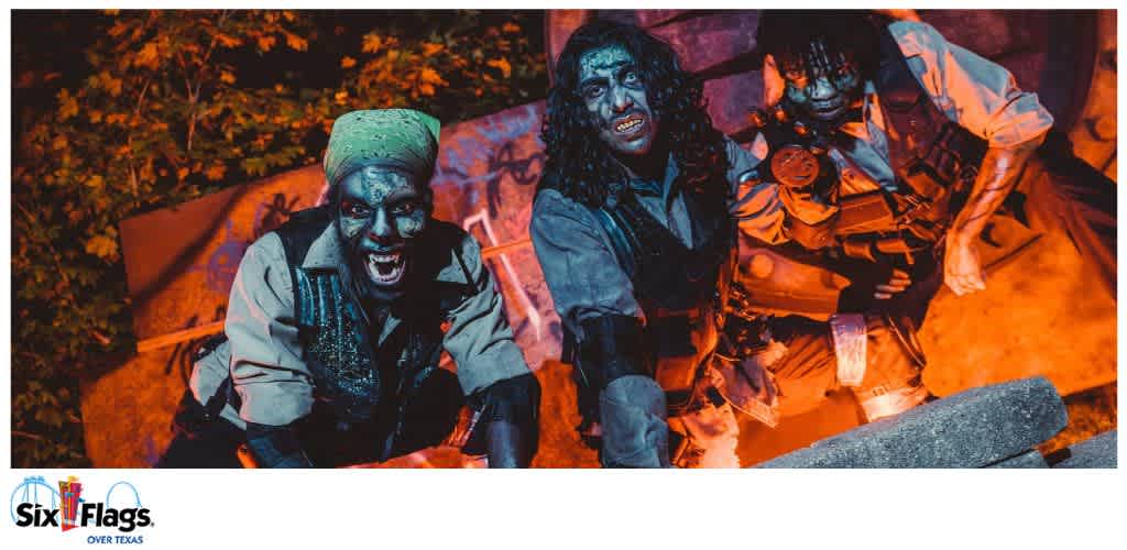 Three individuals in Halloween costumes with dramatic lighting and vegetation in the background.