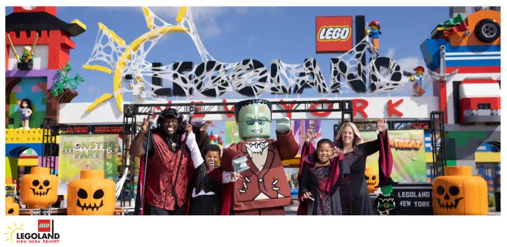 A group in costumes stands in front of the LEGO-themed entrance at LEGOLAND New York Resort during Halloween.