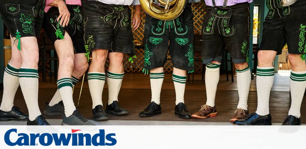 Group of people wearing traditional German attire with socks and shorts, standing indoors on a wooden floor.