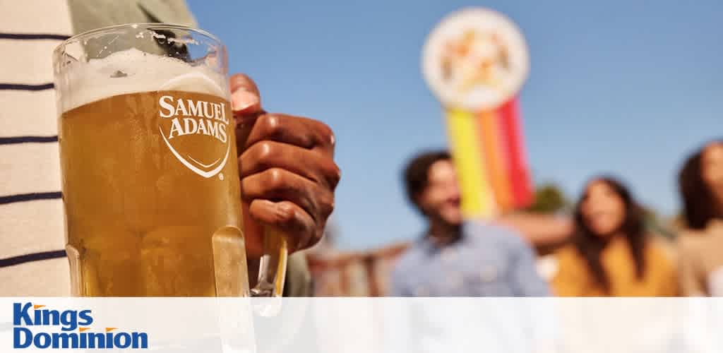 Close-up of a person holding a frosty glass of Samuel Adams beer with a blurred background and Kings Dominion logo.