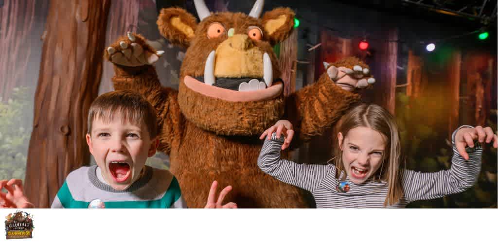 Children wearing excited expressions with a person in a large, furry, monster costume in a festive indoor setting
