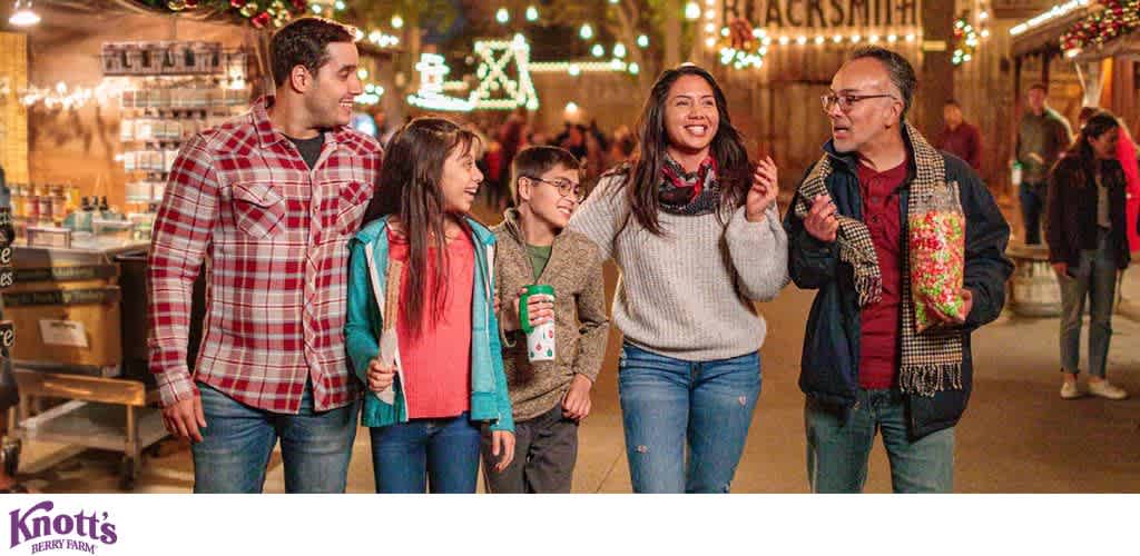 A group of five people walking together outdoors at night with festive holiday lighting in the background.