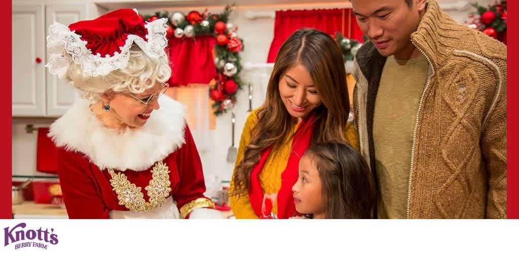 Mrs. Claus interacts with a family in a festive, decorated kitchen setting.
