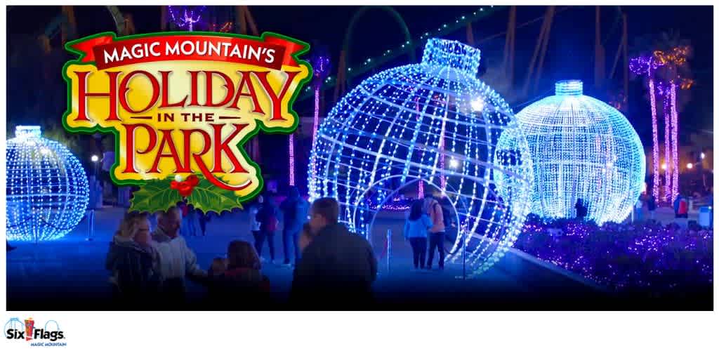A nighttime scene at Six Flags Magic Mountain’s Holiday in the Park, featuring large spherical light displays and people walking beneath them.