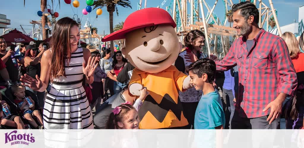 Charlie Brown costume character surrounded by smiling people at an amusement park.